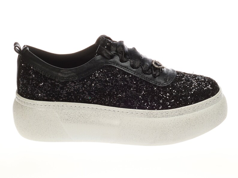 May include: Black glitter sneakers with a white platform sole. The sneakers have a black ribbon lace and a small silver charm on the side.