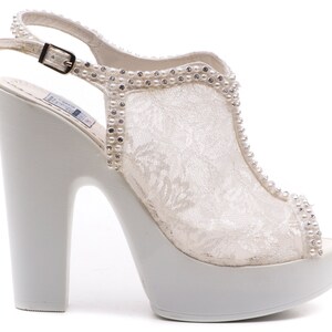 May include: White lace bridal shoes with a platform heel and a rhinestone embellishment around the ankle strap.