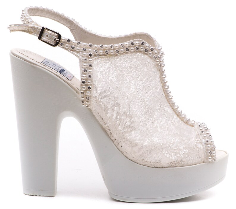 May include: White lace bridal shoes with a platform heel and a rhinestone embellishment around the ankle strap.