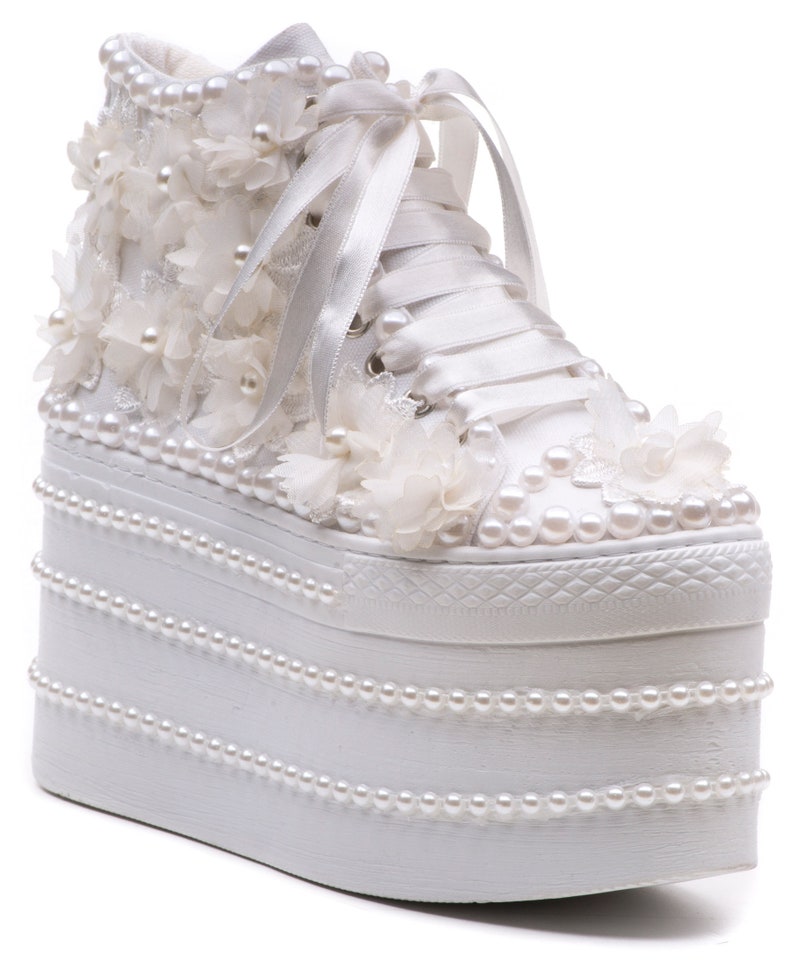 May include: White platform sneakers with a high top, embellished with pearl beads and white fabric flowers. The laces are white satin ribbon.