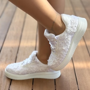 May include: White sneakers with lace detailing and a white sole. The sneakers are covered in white lace and have a delicate floral pattern.