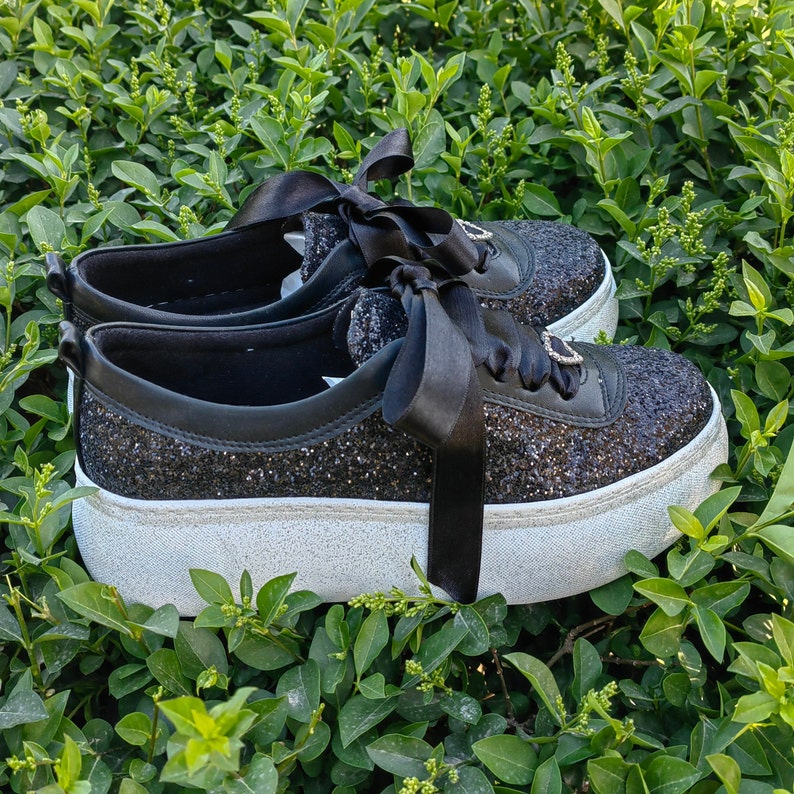 May include: Black glitter platform sneakers with black satin ribbon laces. The sneakers have a white platform sole.