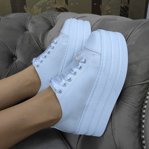 May include: White platform sneakers with a satin ribbon detail and a small rhinestone embellishment.