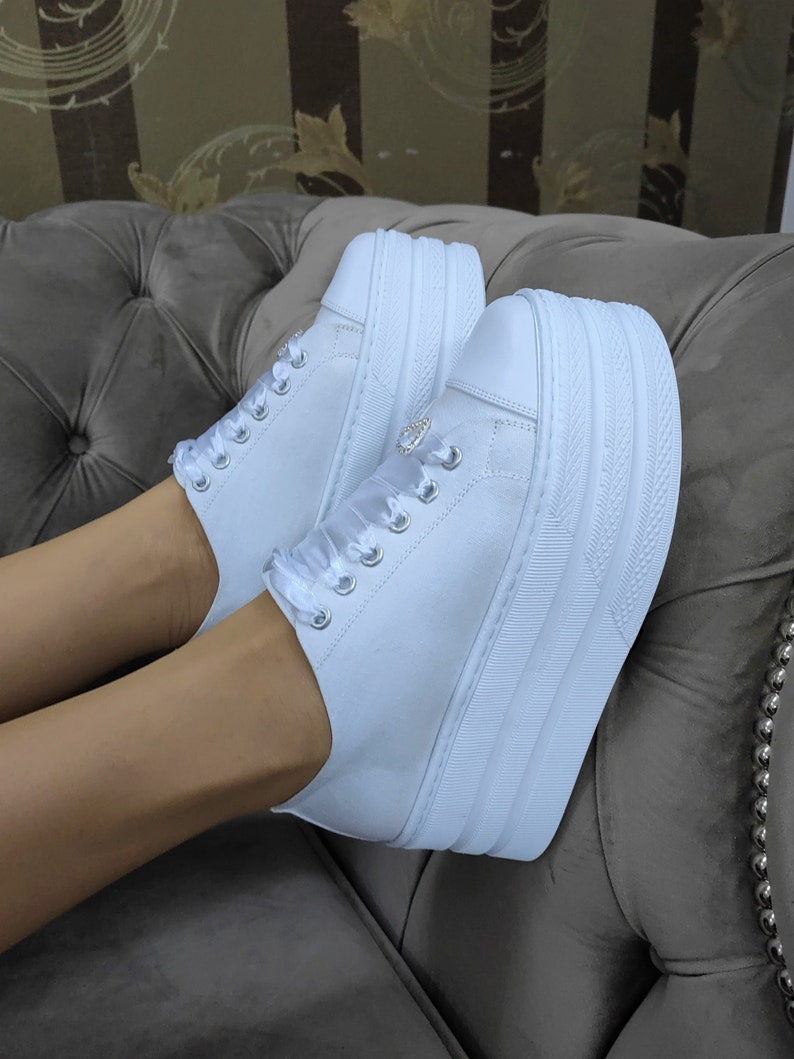 May include: White platform sneakers with a satin ribbon detail and a small rhinestone embellishment.