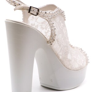 May include: White lace bridal heels with a platform sole and a buckle closure. The heels are decorated with pearl-like embellishments.
