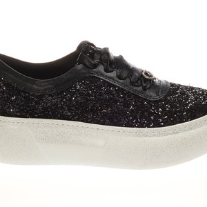 May include: Black glitter sneakers with a white platform sole. The sneakers have a black ribbon lace and a small silver charm on the side.