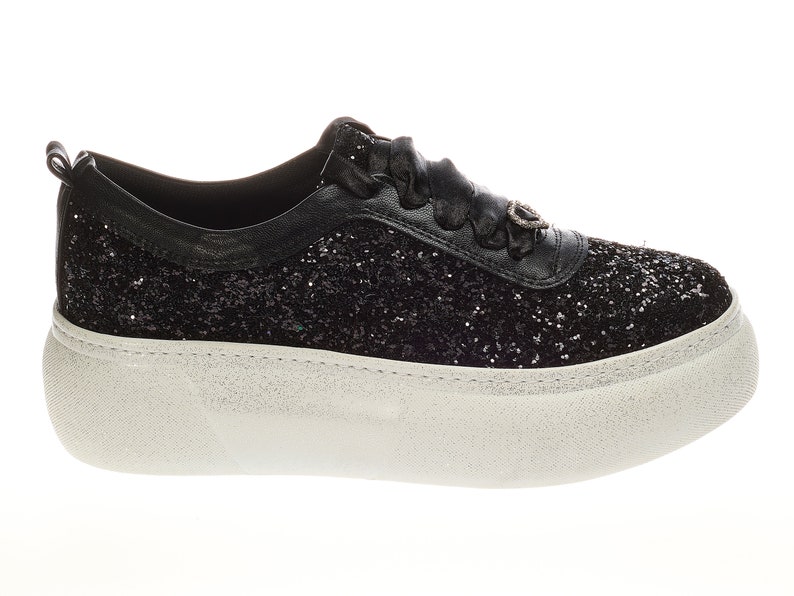 May include: Black glitter sneakers with a white platform sole. The sneakers have a black ribbon lace and a small silver charm on the side.