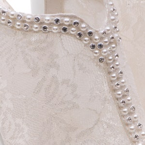 May include: White lace fabric with a beaded trim. The trim is made of small white pearls and clear rhinestones.