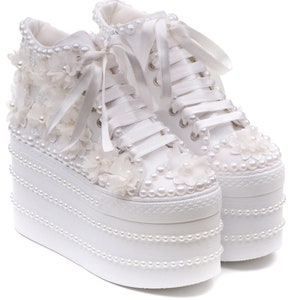May include: White platform sneakers with pearl embellishments and lace detailing. The shoes have a high platform and are decorated with pearls and lace flowers.