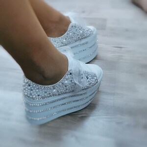 May include: White platform sneakers with a satin finish and embellished with pearls and rhinestones.
