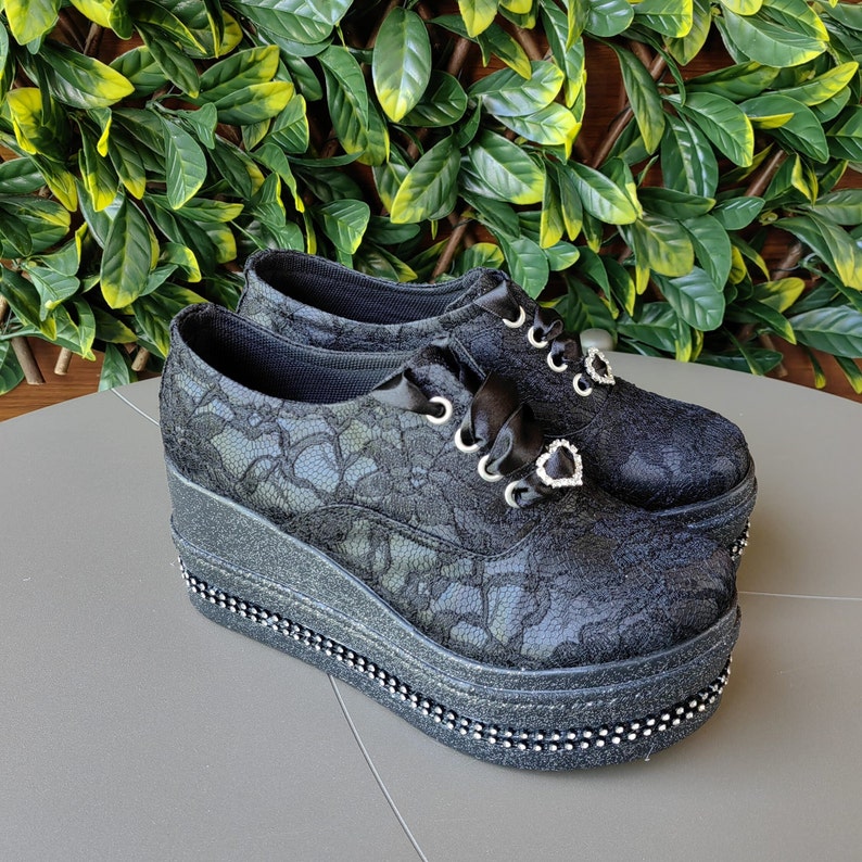 May include: Black lace platform shoes with a chunky heel and a heart-shaped rhinestone embellishment.