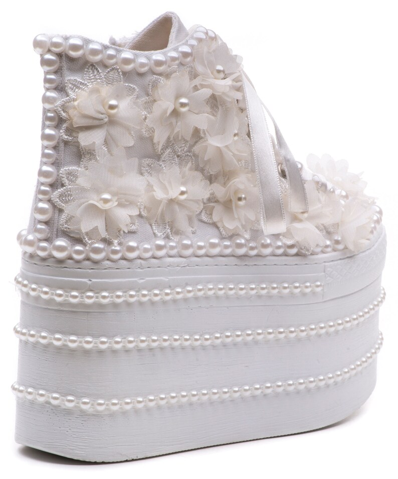 May include: White platform sneakers with a high platform sole decorated with pearl beads and white fabric flowers.