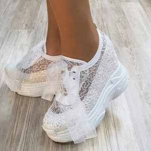 May include: White lace sneakers with a platform sole and a white ribbon bow. The sneakers are decorated with glitter.