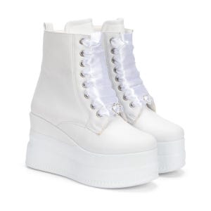 Könnte beinhalten: Weiße Plateau-Stiefel mit Schnürdesign und weißen Band-Schnürsenkeln. Die Stiefel haben eine klobige Plateausohle und sind mit herzförmigen Verzierungen versehen. Die Stiefel sind aus glattem, weißem Material.