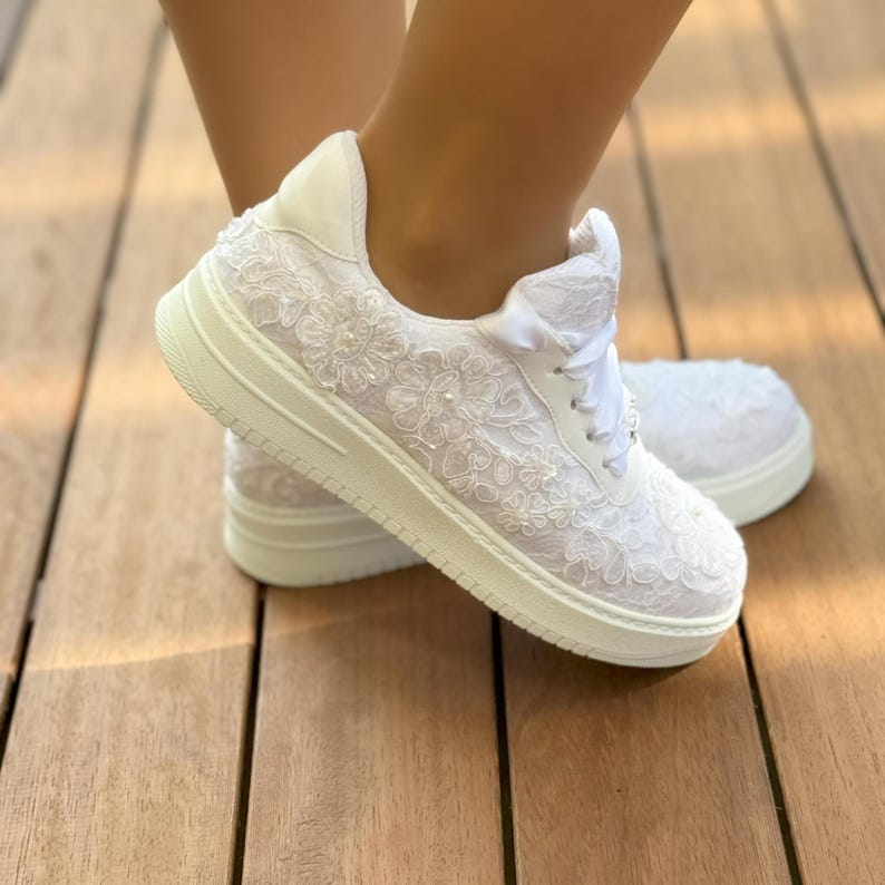 May include: White lace sneakers with a white satin ribbon and a white sole. The sneakers are decorated with white lace and pearls.