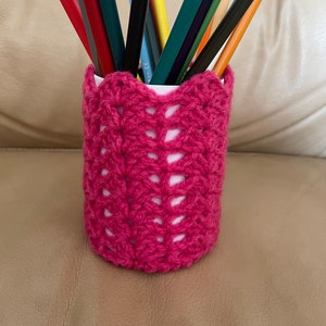 Peut inclure: Un porte-crayons en crochet rose avec une variété de crayons de couleur à l'intérieur.