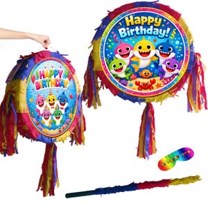 May include: Two colorful piñatas with a "Happy Birthday!" design featuring cartoon sharks. The piñatas are round with fringed edges in red, yellow, and blue. A rainbow-colored party mask and a stick are also included.