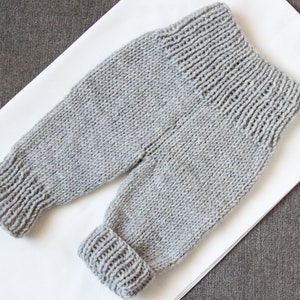 May include: Grey knitted baby trousers with a fold-over cuff at the ankles.
