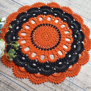 May include: A round, handmade crochet doily featuring alternating concentric rings of vibrant orange and deep black yarn. The intricate design includes a central starburst pattern, delicate openwork loops, and a scalloped edge with detailed stitching.