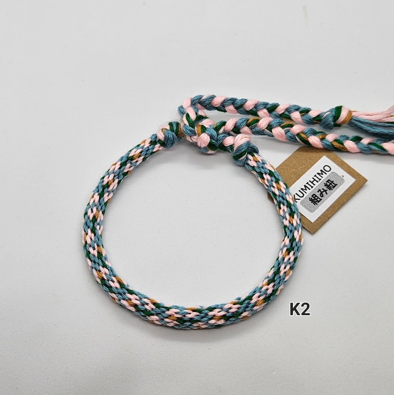 May include: A braided bracelet with blue, pink, and green threads. The bracelet is tied with a knot and has a small tag that says "KUMIHIMO 組み紐".