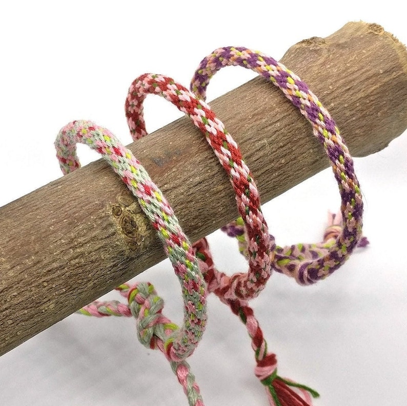 May include: Three colorful friendship bracelets made with woven thread in pink, green, and purple.