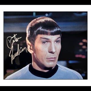 Peut inclure: Photographie encadrée d'un homme aux oreilles pointues et à la coiffure sombre et courte. L'image comprend un autographe à l'encre argentée. L'homme porte un uniforme bleu.