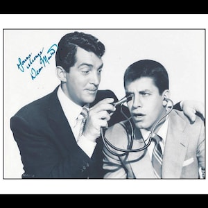 Peut inclure: Photographie en noir et blanc de Dean Martin et Jerry Lewis. Dean Martin tient un appareil près de l'œil de Jerry Lewis. La photo comporte un autographe dans le coin supérieur gauche. Les deux hommes portent des costumes et des cravates.