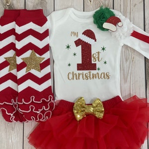 Pu&ograve; includere: Un completo natalizio festivo per neonati, con un body bianco con "My 1st Christmas" in lettere dorate e un motivo a cappello di Babbo Natale. Include una gonna tutu rossa con un fiocco di paillettes dorate, scaldamuscoli a righe rosse e bianche e un accessorio per capelli verde e bianco.
