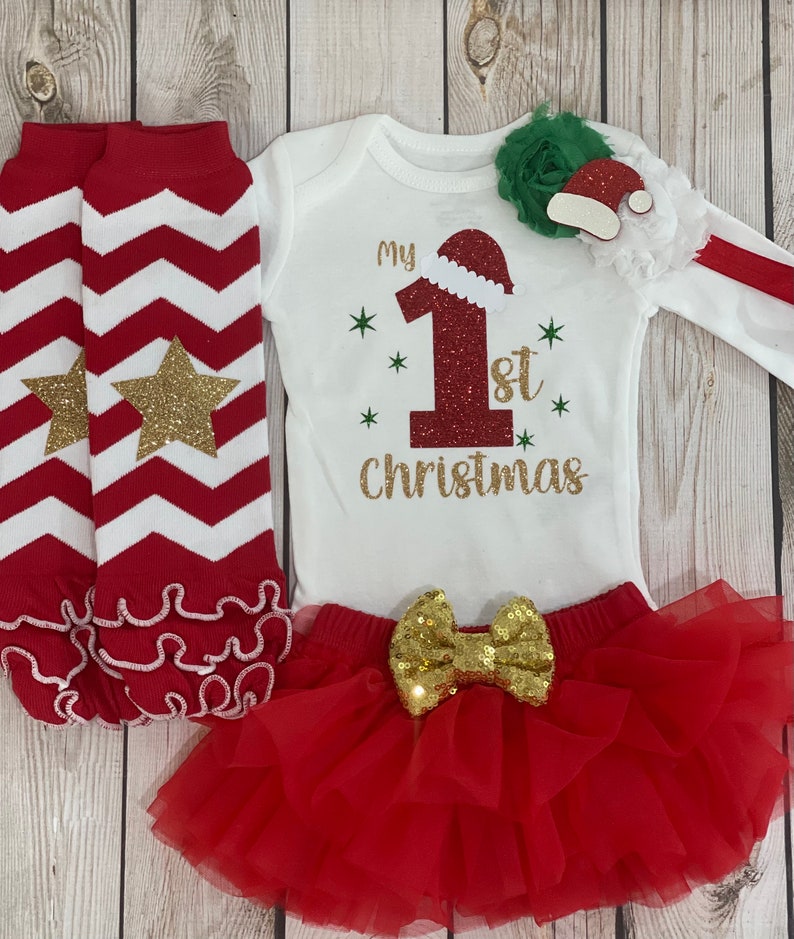Pu&ograve; includere: Un completo natalizio festivo per neonati, con un body bianco con "My 1st Christmas" in lettere dorate e un motivo a cappello di Babbo Natale. Include una gonna tutu rossa con un fiocco di paillettes dorate, scaldamuscoli a righe rosse e bianche e un accessorio per capelli verde e bianco.