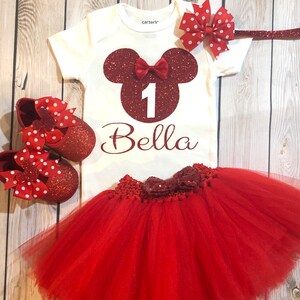 Puede incluir: Conjunto de primer cumplea&ntilde;os de Minnie Mouse rojo y blanco para una ni&ntilde;a. El conjunto incluye un body blanco con una cabeza de Minnie Mouse roja con purpurina, el n&uacute;mero uno y el nombre Bella. El conjunto tambi&eacute;n incluye un tut&uacute; rojo de tul con un lazo rojo con purpurina, una diadema roja con purpurina con un lazo rojo y blanco de lunares y zapatos rojos con purpurina con lazos rojos y blancos de lunares.
