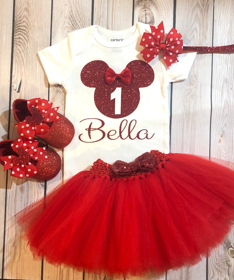 Puede incluir: Conjunto de primer cumplea&ntilde;os de Minnie Mouse rojo y blanco para una ni&ntilde;a. El conjunto incluye un body blanco con una cabeza de Minnie Mouse roja con purpurina, el n&uacute;mero uno y el nombre Bella. El conjunto tambi&eacute;n incluye un tut&uacute; rojo de tul con un lazo rojo con purpurina, una diadema roja con purpurina con un lazo rojo y blanco de lunares y zapatos rojos con purpurina con lazos rojos y blancos de lunares.