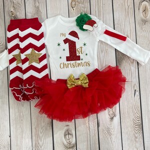 Pu&ograve; includere: Un completo festivo per neonati per il primo Natale. Il set include un body bianco a maniche lunghe con la scritta "My 1st Christmas", una gonna tutu rossa, scaldamuscoli a zig-zag rossi e bianchi con stelle dorate e una fascia con cappello di Babbo Natale.