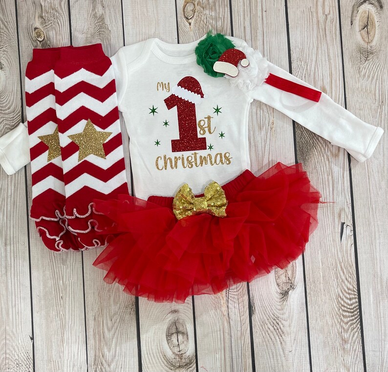 Pu&ograve; includere: Un completo festivo per neonati per il primo Natale. Il set include un body bianco a maniche lunghe con la scritta "My 1st Christmas", una gonna tutu rossa, scaldamuscoli a zig-zag rossi e bianchi con stelle dorate e una fascia con cappello di Babbo Natale.