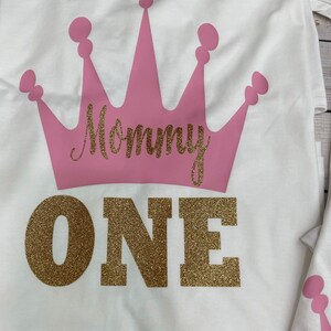 May include: White t-shirt with a pink crown and the words "Mommy One" in gold glitter.