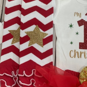 Pu&ograve; includere: Un completo festivo per neonati con scaldamuscoli a zig-zag rossi e bianchi con stelle glitterate dorate, un body bianco con "My 1st Christmas" in glitter dorati e un tut&ugrave; rosso. Il completo &egrave; pensato per il primo Natale di un bambino.