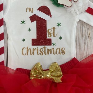 Pu&ograve; includere: Completo natalizio per neonati con body bianco con scritta "My 1st Christmas" dorata e un "1" rosso glitterato con cappello da Babbo Natale. Include gonna tutu rossa con fiocco dorato e fascia abbinata.