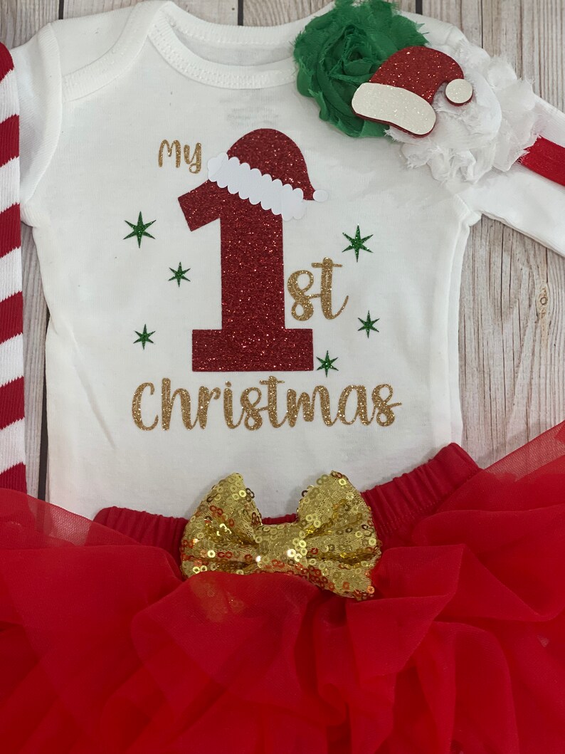 Pu&ograve; includere: Completo natalizio per neonati con body bianco con scritta "My 1st Christmas" dorata e un "1" rosso glitterato con cappello da Babbo Natale. Include gonna tutu rossa con fiocco dorato e fascia abbinata.