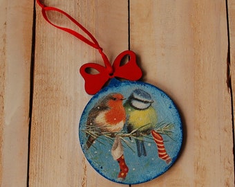 May include: A blue and white Christmas ornament with a red bow and two birds perched on a branch. The birds are a bluebird and a robin.
