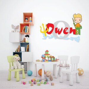 May include: A white play table with two white chairs and a wooden block tower. The wall behind the table has a red, yellow, and blue wooden name sign that says "Owen" with a cartoon superhero holding a trident.
