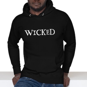May include: A black hooded sweatshirt with the word "WICKED" printed in white on the front. The model is wearing blue jeans.
