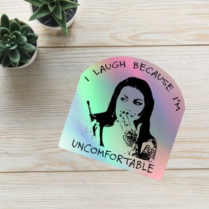 May include: A holographic sticker with a black and white illustration of a woman with a hand over her mouth. The text on the sticker reads "I laugh because I'm uncomfortable".