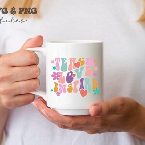Peut inclure: Une tasse en c&eacute;ramique blanche avec un motif color&eacute; qui dit "Teach Love Inspire" dans une police r&eacute;tro. Le motif comprend des fleurs, des c&oelig;urs et des &eacute;toiles.