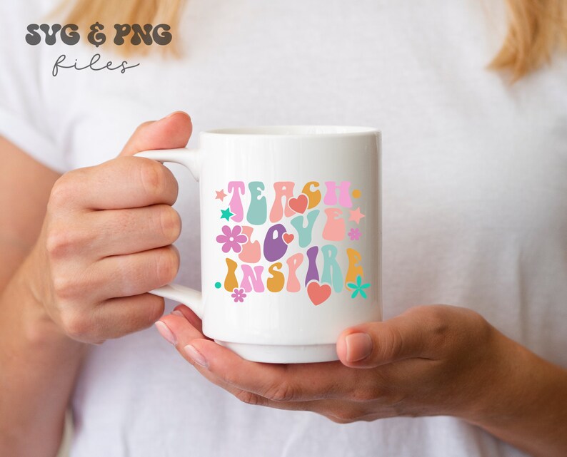 Peut inclure: Une tasse en c&eacute;ramique blanche avec un motif color&eacute; qui dit "Teach Love Inspire" dans une police r&eacute;tro. Le motif comprend des fleurs, des c&oelig;urs et des &eacute;toiles.