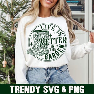 Puede incluir: Sudadera blanca con un gr&aacute;fico circular verde que dice "LIFE IS BETTER IN THE GARDEN". El gr&aacute;fico presenta dos botas de agua verdes con dise&ntilde;os florales. Debajo del gr&aacute;fico est&aacute; el texto "TRENDY SVG & PNG".