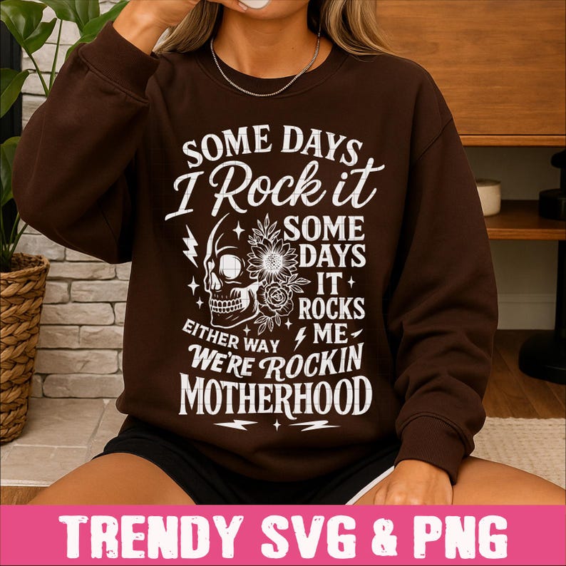 May include: A brown sweatshirt with a white graphic design that says "Some days I rock it, some days it rocks me, either way we're rockin motherhood". The graphic also includes a skull with flowers.