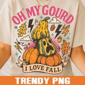 May include: Cream-colored t-shirt featuring a fall-themed graphic. The design includes pumpkins, gourds, acorns, and lightning bolts, with the text "OH MY GOURD" and "I LOVE FALL". The shirt has short sleeves.