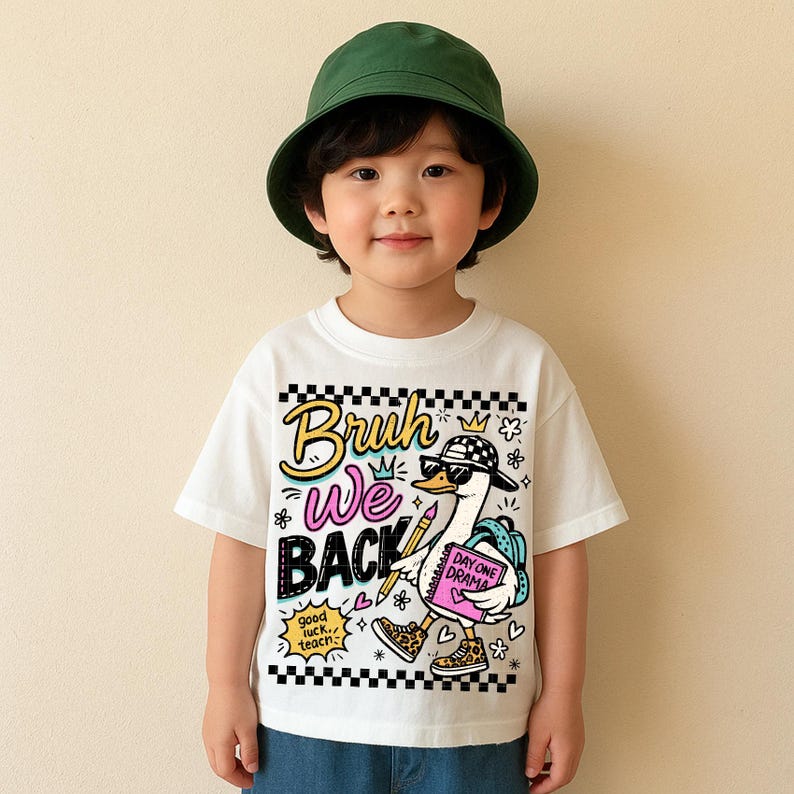 May include: A white t-shirt with a cartoon goose wearing sunglasses, a hat, and sneakers. The shirt has the words "Bruh We Back" in a colorful design. The goose is carrying a book that says "Day One Drama". The child is wearing a green bucket hat.
