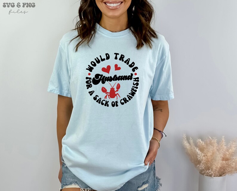 May include: A light blue t-shirt with the text "Would trade a husband for a sack of crawfish" in black with red hearts and a red crawfish illustration.