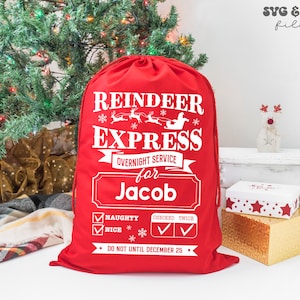 May include: A red drawstring gift sack featuring white text that reads Reindeer Express, Overnight Service for Jacob, Naughty, Nice, Checked Twice, and Do Not Until December 25. The design includes graphics of a sleigh, reindeer, and snowflakes.