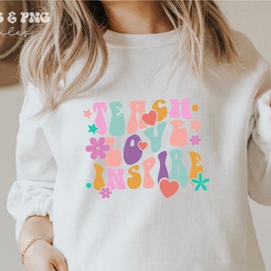 Peut inclure: Sweat-shirt blanc avec un motif graphique color&eacute; qui dit "Teach Love Inspire" dans un style de police r&eacute;tro.